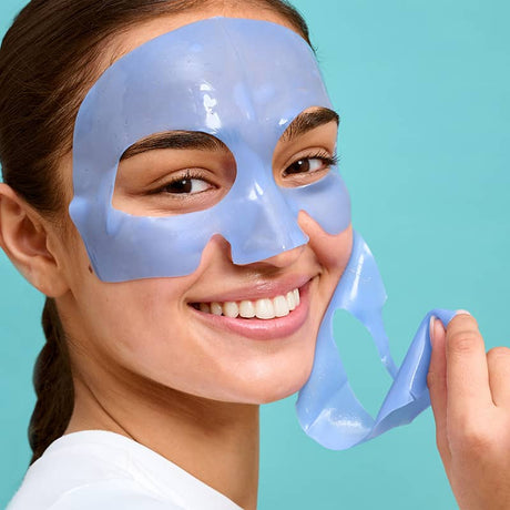 Woman peeling off blue hydrogel sheet face mask, revealing smooth, hydrated skin for a refreshing and revitalizing skincare routine