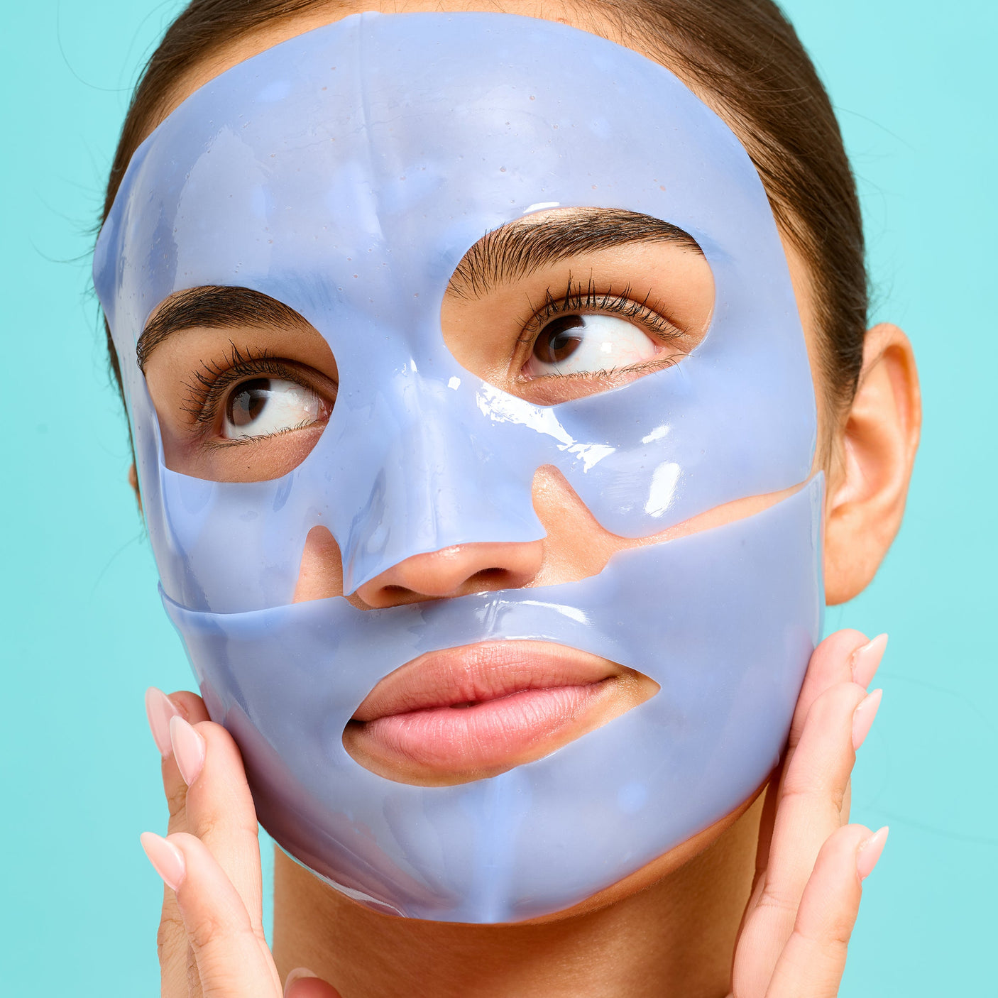 A woman wears a blue Patchology Serve Chilled On Ice sheet mask on her face to firm and de-puff her skin.