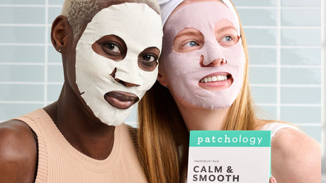 Two women wearing different colored sheet masks pose together while holding a Patchology “Calm & Smooth” SmartMud Duo box, highlighting a soothing and smoothing skincare treatment.