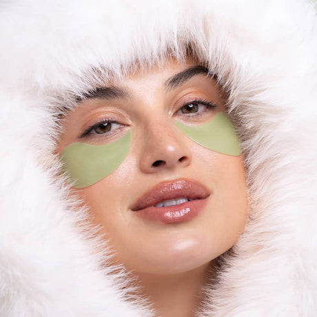 Woman wearing green eye patches with a white fuzzy hood