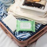 Open suitcase with clothes, sunglasses, wallet, and a packet of 'Clean AF' wipes.